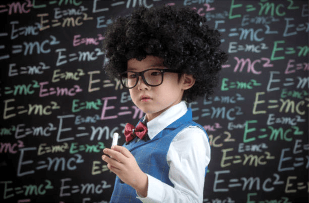A young child wearing a curly wig, glasses, and a bow tie poses confidently in front of a blackboard covered with colorful "E=mc²" equations, embodying the playful spirit often seen in early learning centres.