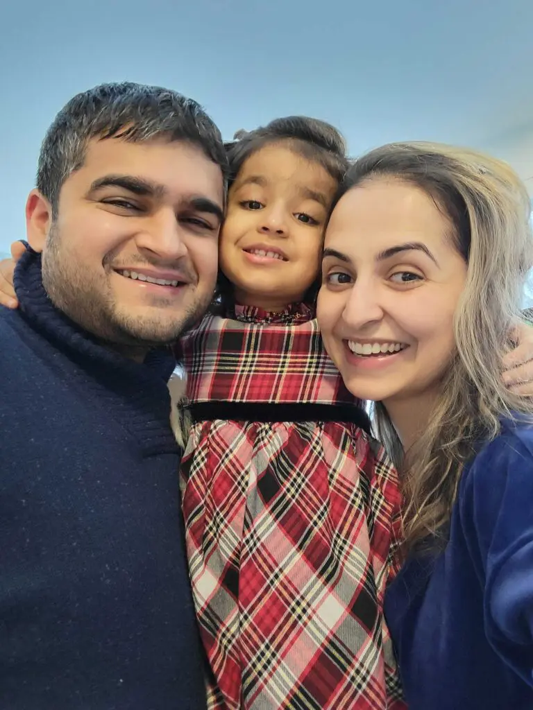 A smiling man, woman, and young girl stand close together, posing for a cheerful selfie. The girl, wearing a red and black plaid dress, is hugged by both adults—all likely enjoying time after visiting early learning centres nearby.