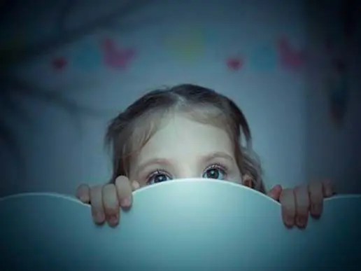 A young child peeks over a light-colored surface, with only their eyes and fingers visible. The softly blurred background evokes the warm, nurturing environment found in top early learning centres.
