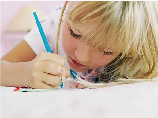 A young girl with blonde hair is lying down and writing with a blue pen on a piece of paper, focusing intently—a scene often seen at early learning centres.