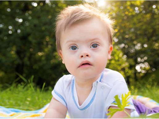 A baby with light brown hair and blue eyes lies on a blanket outside, looking up with curiosity. Sunlight filters through the trees in the background—a scene that inspires many early learning centres and courses on early childhood education.