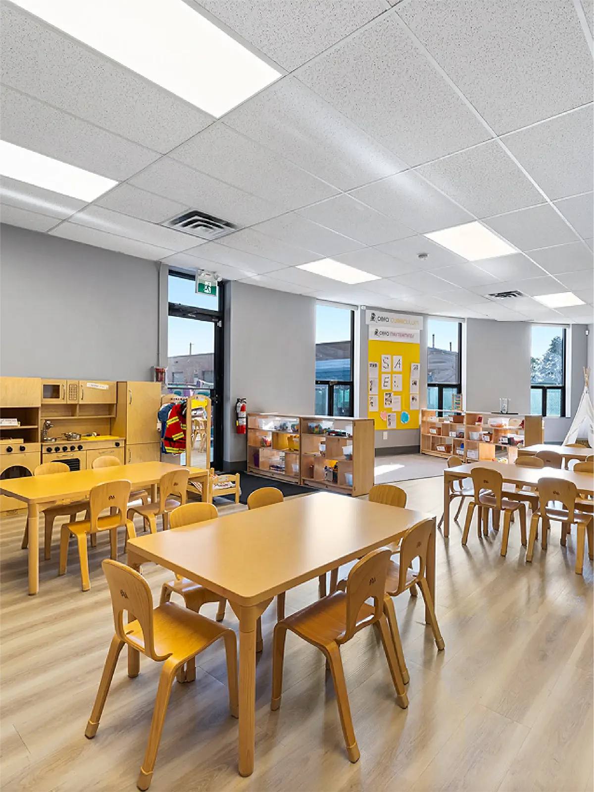 A bright classroom in one of the top early learning centres, with light wood tables and chairs, shelves of educational toys, large windows, and children’s artwork on the walls creates a clean, organized, and inviting space for preschoolers.