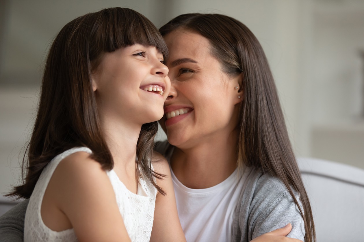 A woman and a young girl smiling and embracing each other, sitting close together. Their joy reflects the nurturing environment found in quality early learning centres, where children thrive with caring support.