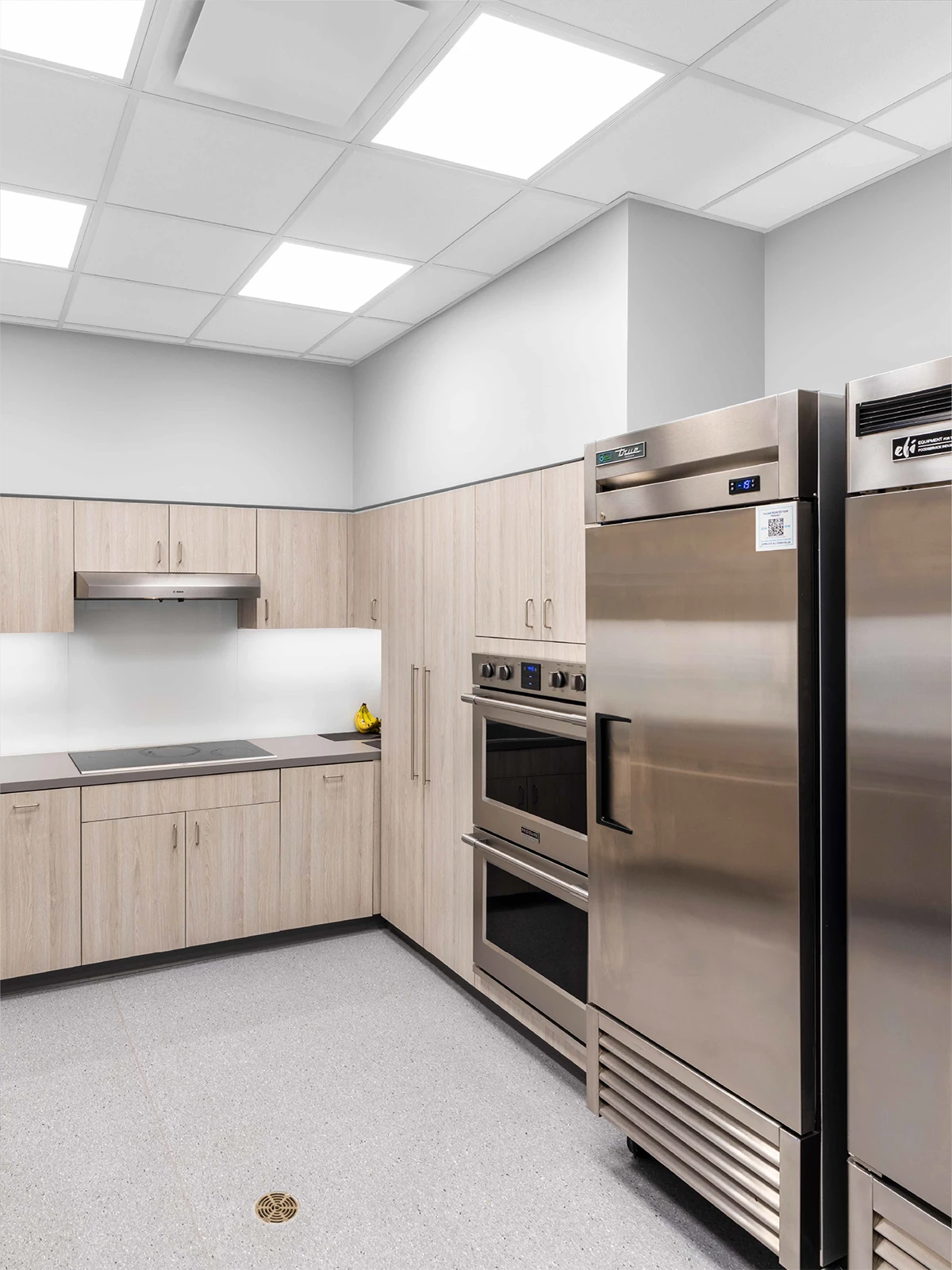Modern kitchen with light wood cabinets, double wall ovens, and sleek appliances—an ideal setup for early learning centres or preschools close to me to teach kids simple cooking lessons in a clean, minimalist space.