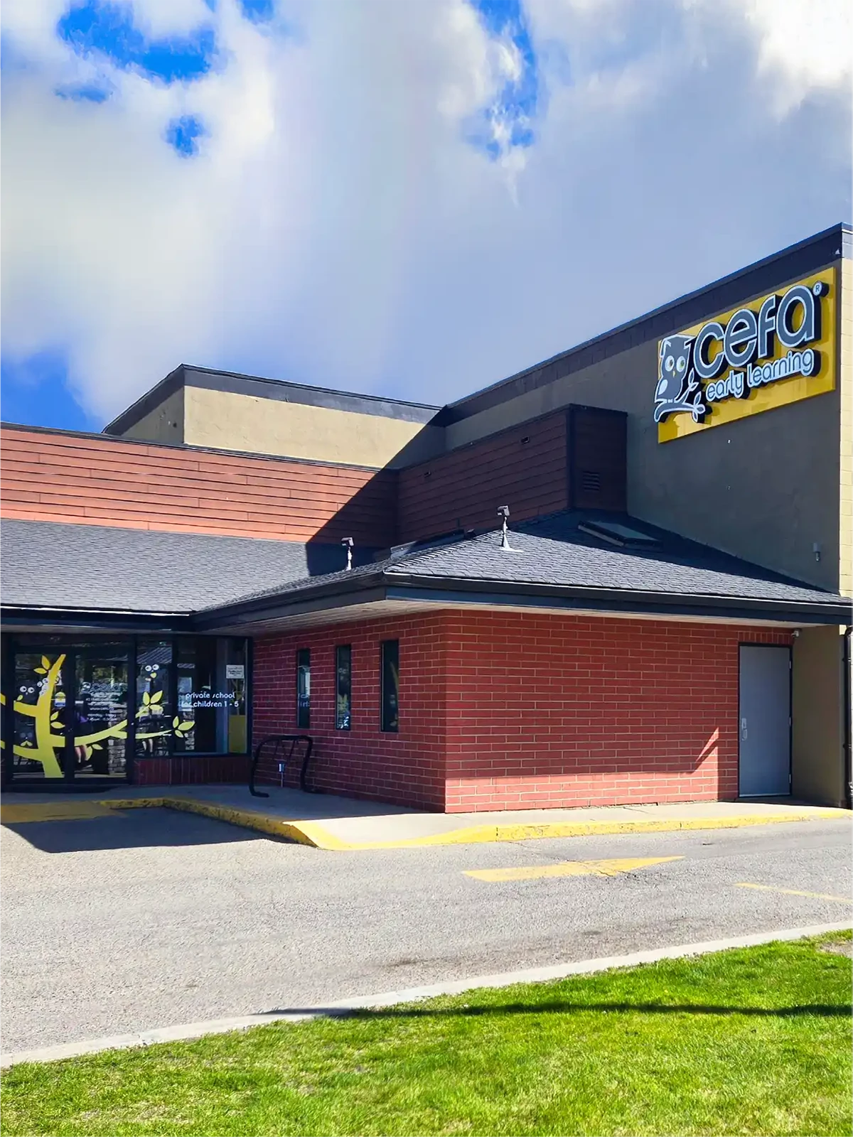 Single-story building with a brick and beige exterior under a partly cloudy sky. A large “CEFA Early Learning” sign marks it as one of the top early learning centres, with playful children’s graphics on the windows and grass and pavement in front.