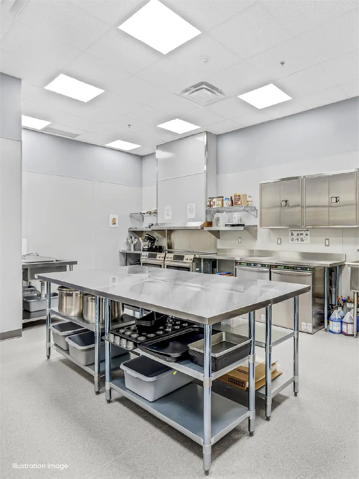 A commercial kitchen, ideal for early learning centres, with stainless steel work tables, shelves stocked with containers and utensils, metal cabinets, an oven, and various appliances under bright overhead lights.
