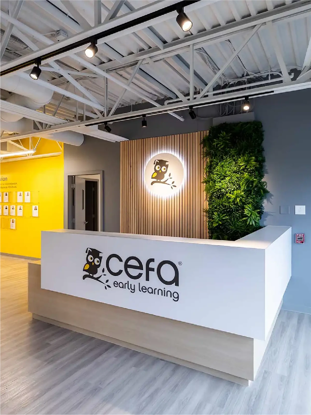 Reception area of a CEFA early learning centre, featuring a white desk with the CEFA logo, lush green plant wall, wooden accents, and a brightly lit modern interior—perfect for families searching for preschools close to me.