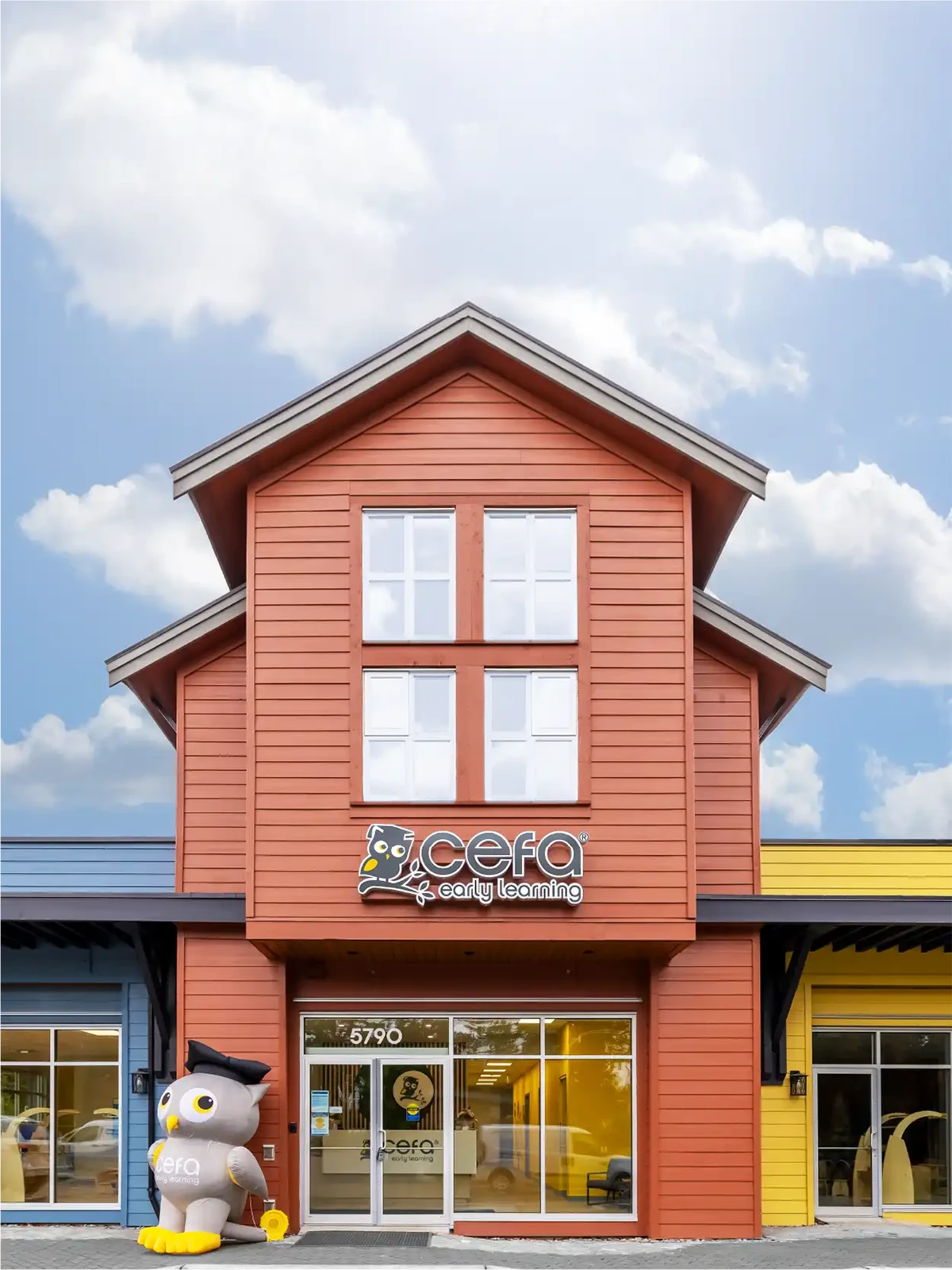 A bright red building with large windows features the "CEFA Early Learning" sign above the entrance, highlighting one of the top early learning centres. A large penguin statue with a graduation cap stands outside, beneath a bright blue sky.